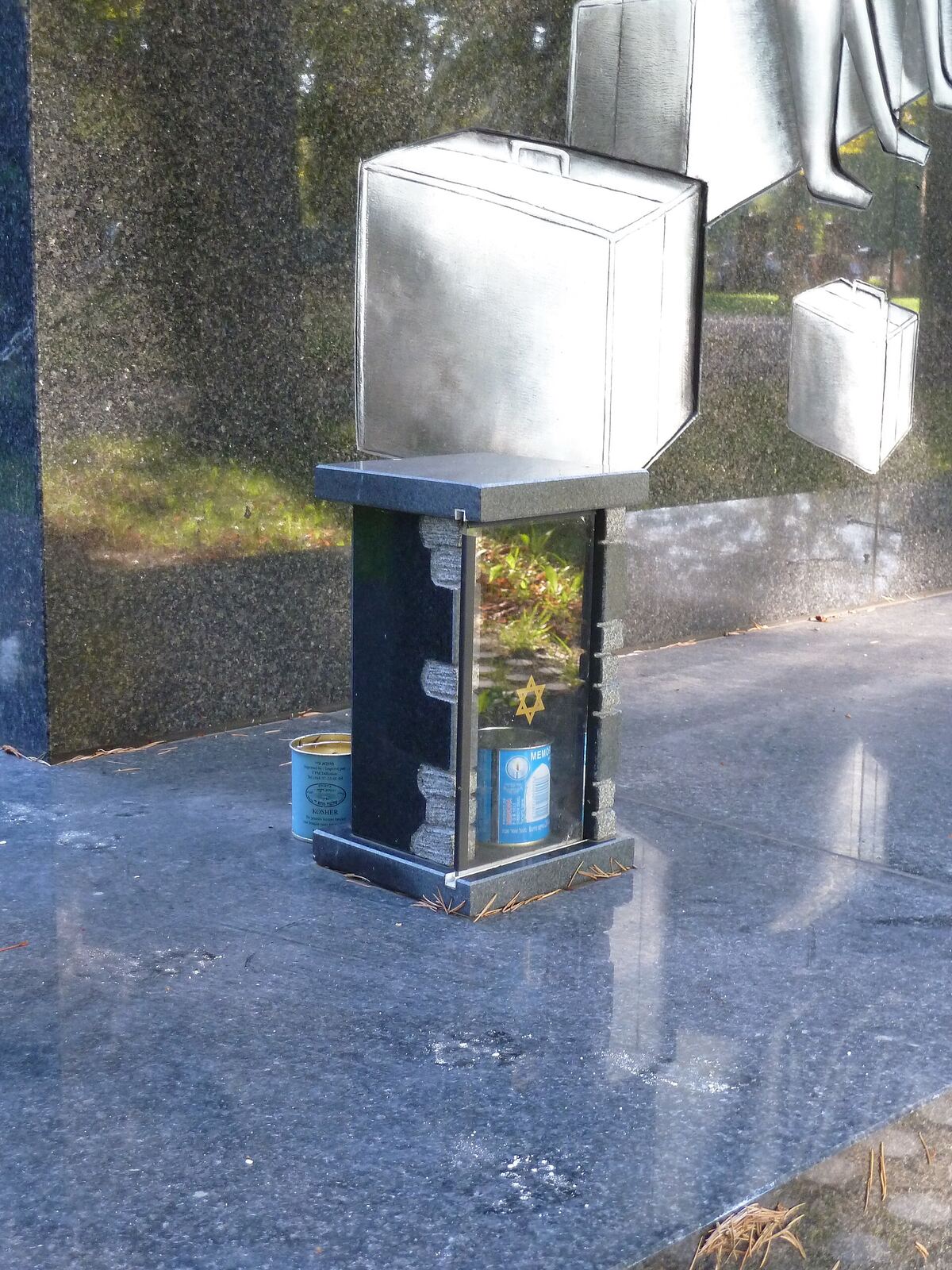 A sculpture at the Algerian Jewish Memorial in Paris shows a suitcase on containers with plants, representing remembrance.
