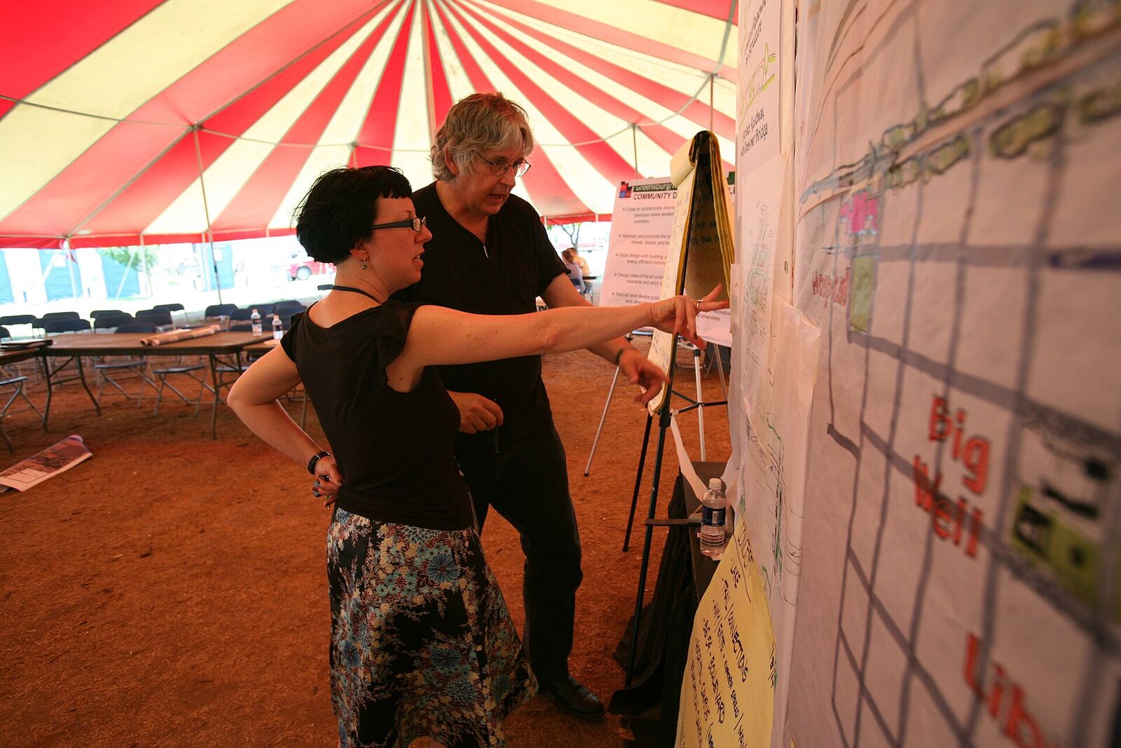 Outdoor Event | The Life After Tragedy Two people discuss a large map under a tent, illustrating community support after loss.