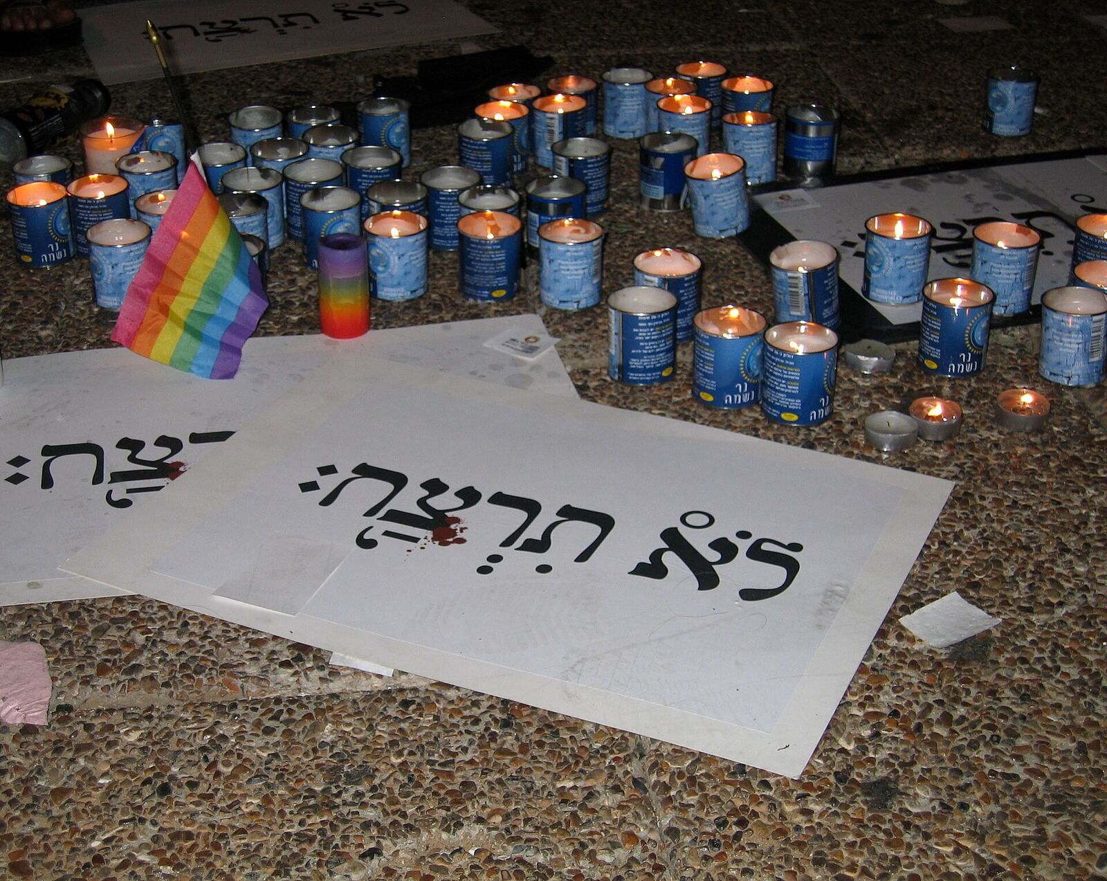 Candles and signs commemorate victims at a vigil for LGBTQ+ rights in Israel, offering grief support after tragedy.
